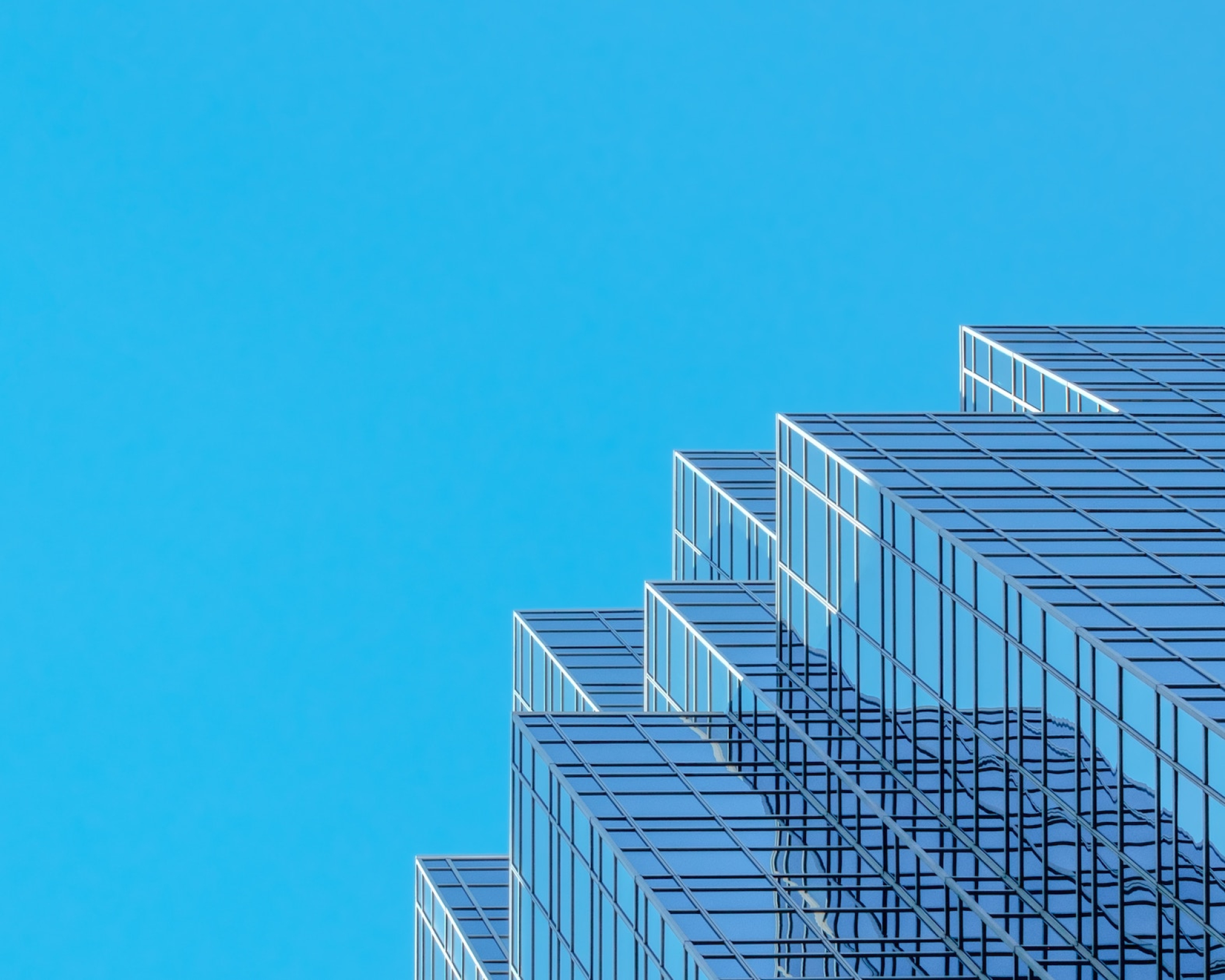 Upward view of glass windows of skyscraper against clear blue sky