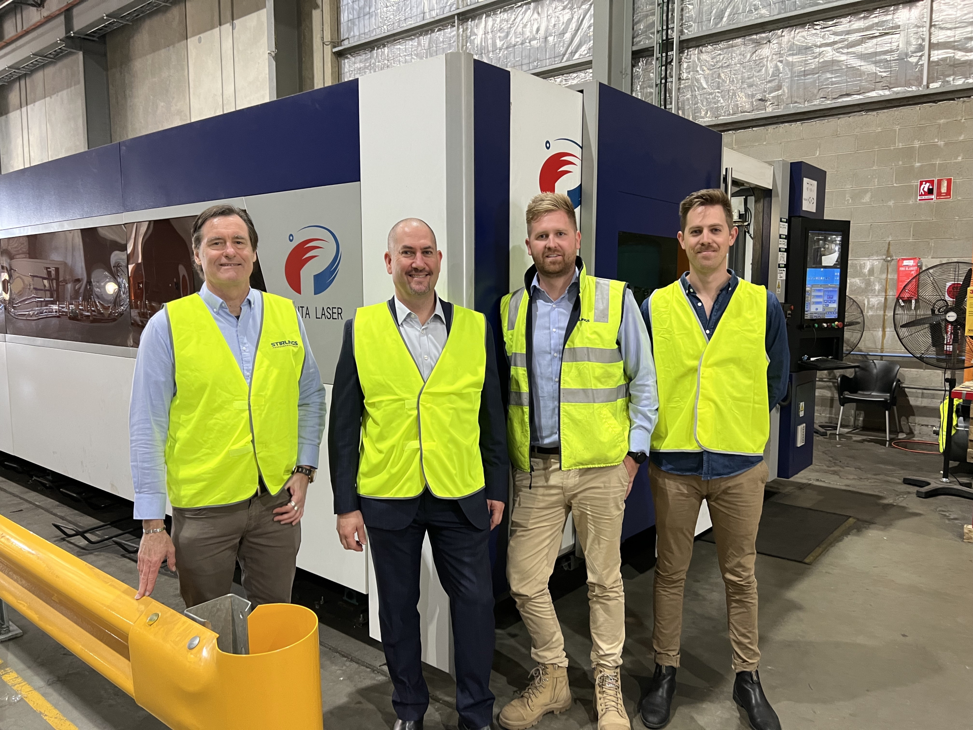 4 men in high vis vests standing in front of a Penta Bolt Laser Cutter. They are smiling.