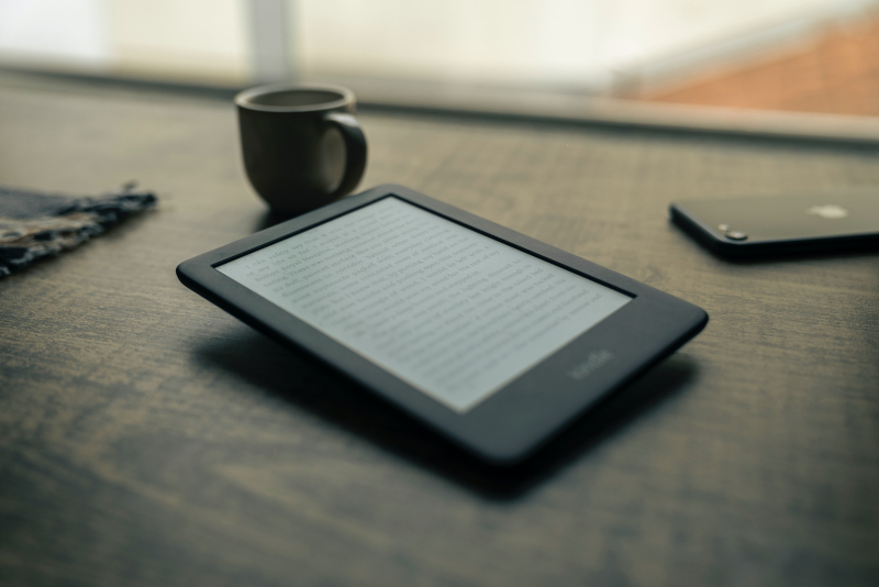 Kindle on a table with a coffee and phone in the background.