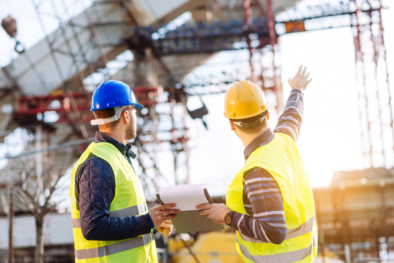 Two construction workers pointing towards a construction site.