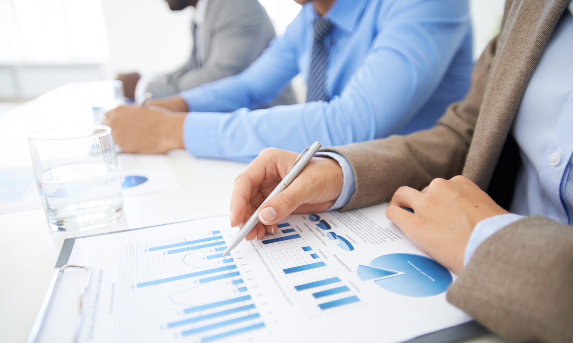 Folder with bar graphs and pie charts and person with pen in hand working on the page.