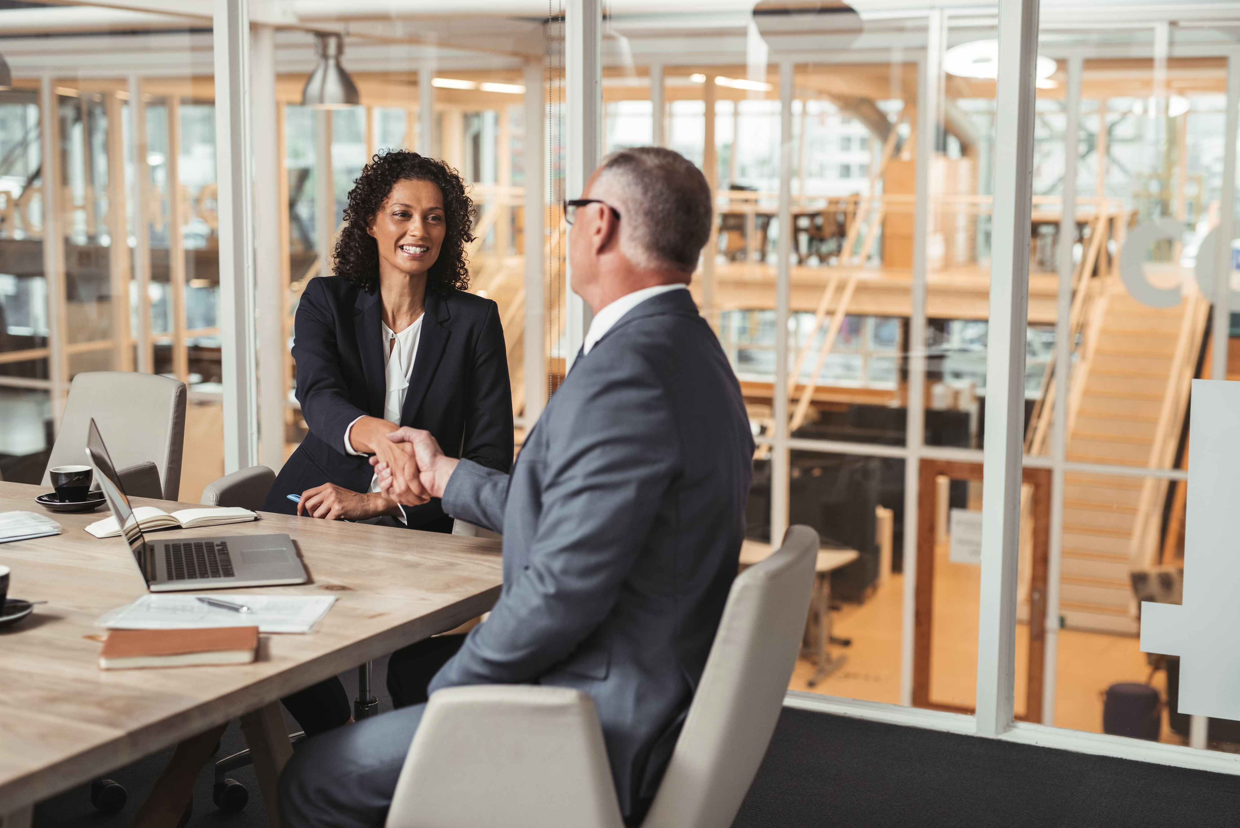 Two business people shaking hands at a desk.