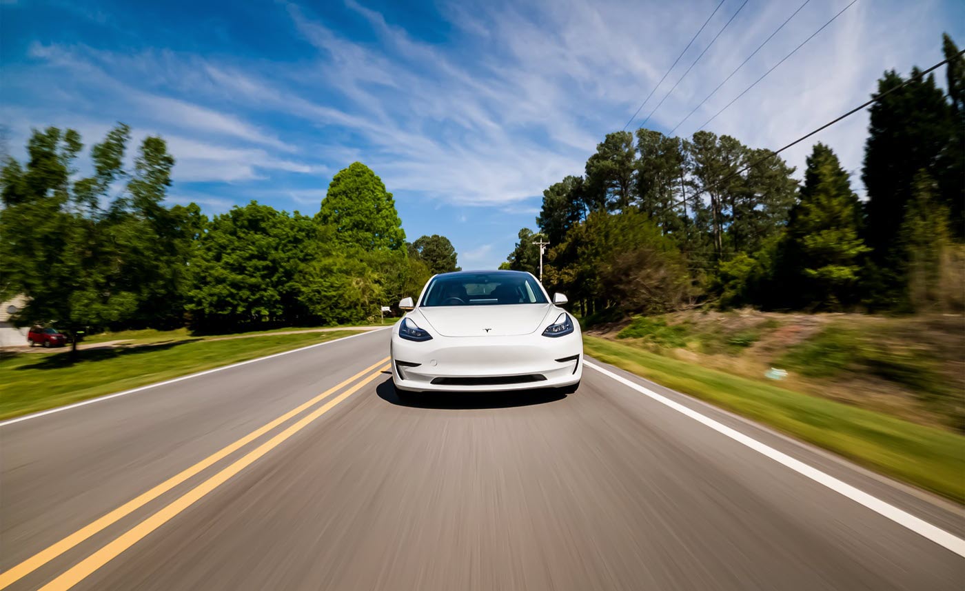 A white model 3 Tesla driving down the road, powered by lithium batteries.